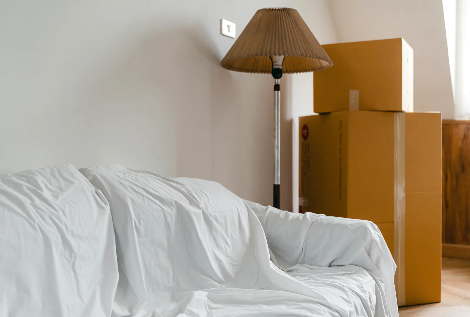 Heller Wohnraum mit abgedecktem Sofa und gepackten Umzugskartons